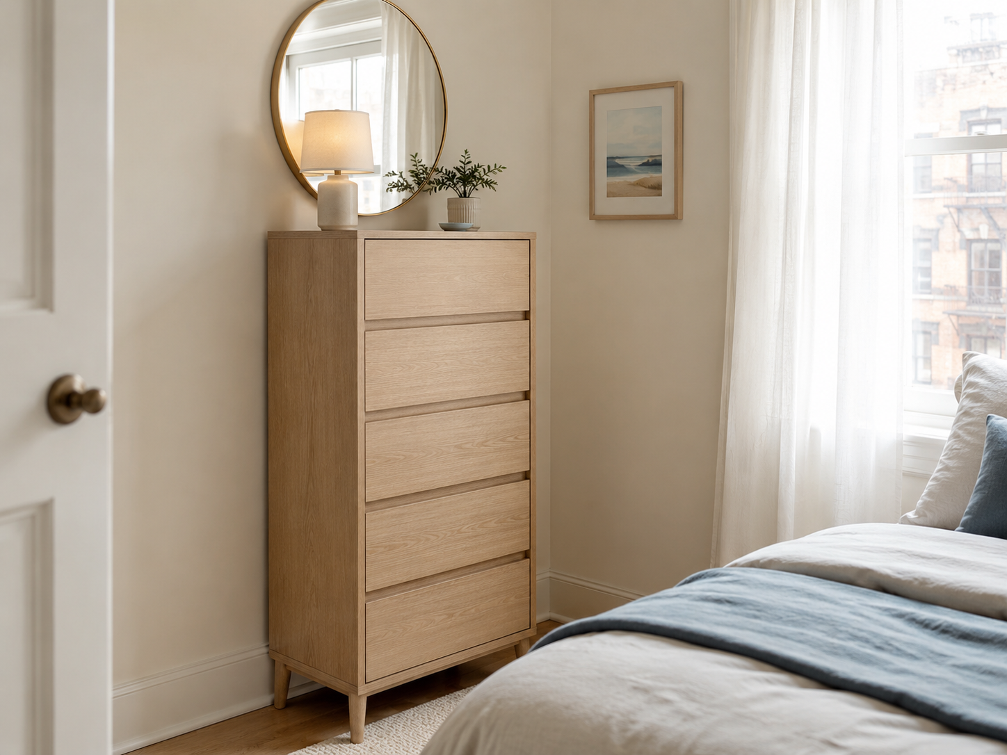 Apartment bedroom with a slim tall dresser, round mirror, lamp, tiny plant, compact bed or curtain, and pale oak accents