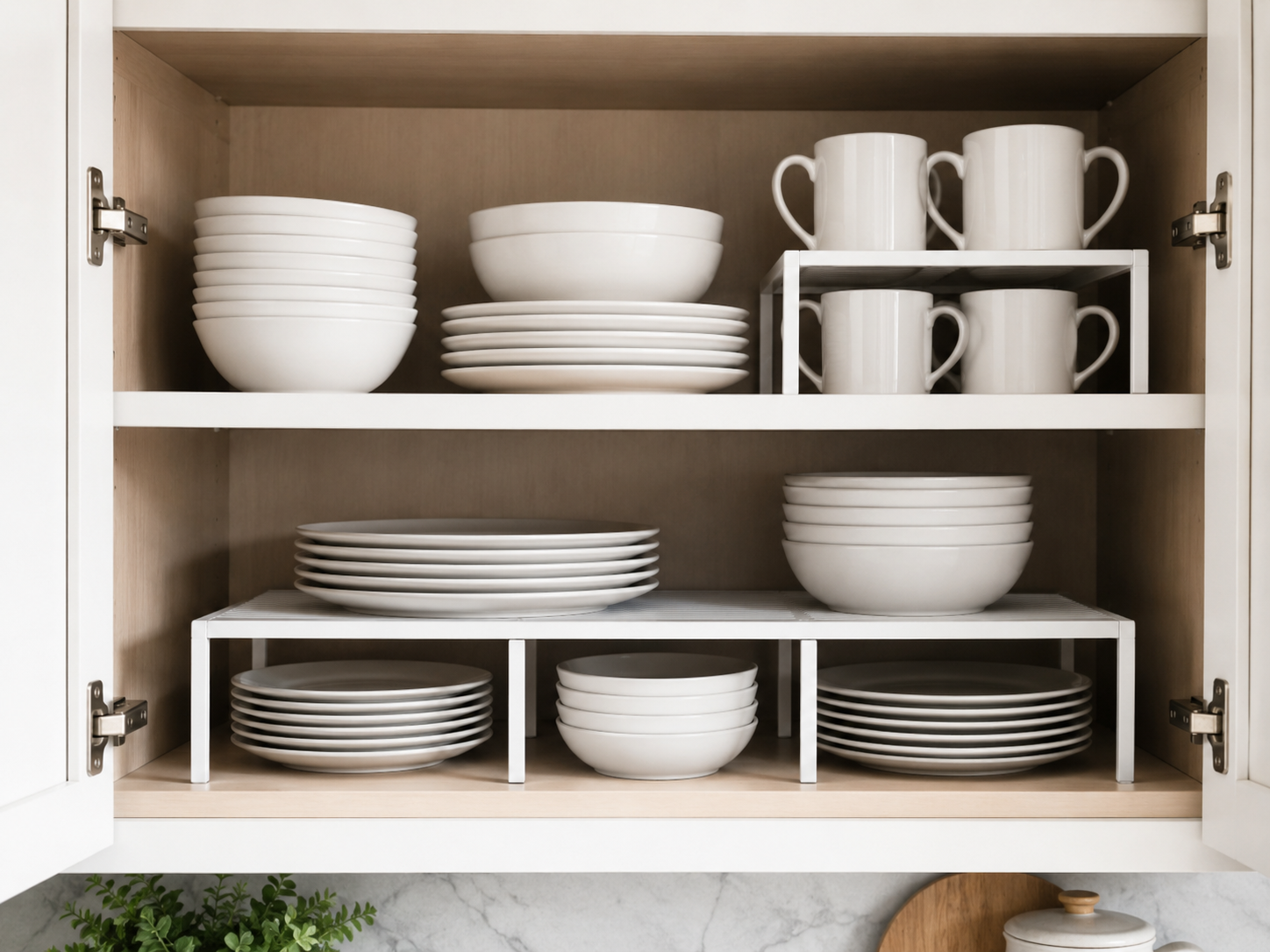 Inside modern kitchen cabinet with shelf risers organizing white plates, bowls, mugs, and neutral dishware