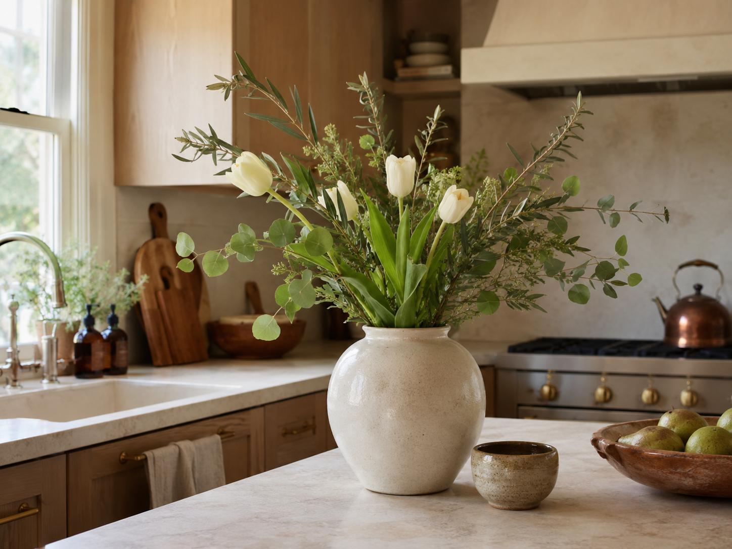 Ceramic vase with simple seasonal flowers or branches on a cozy kitchen counter with warm neutral cabinets and soft daylight