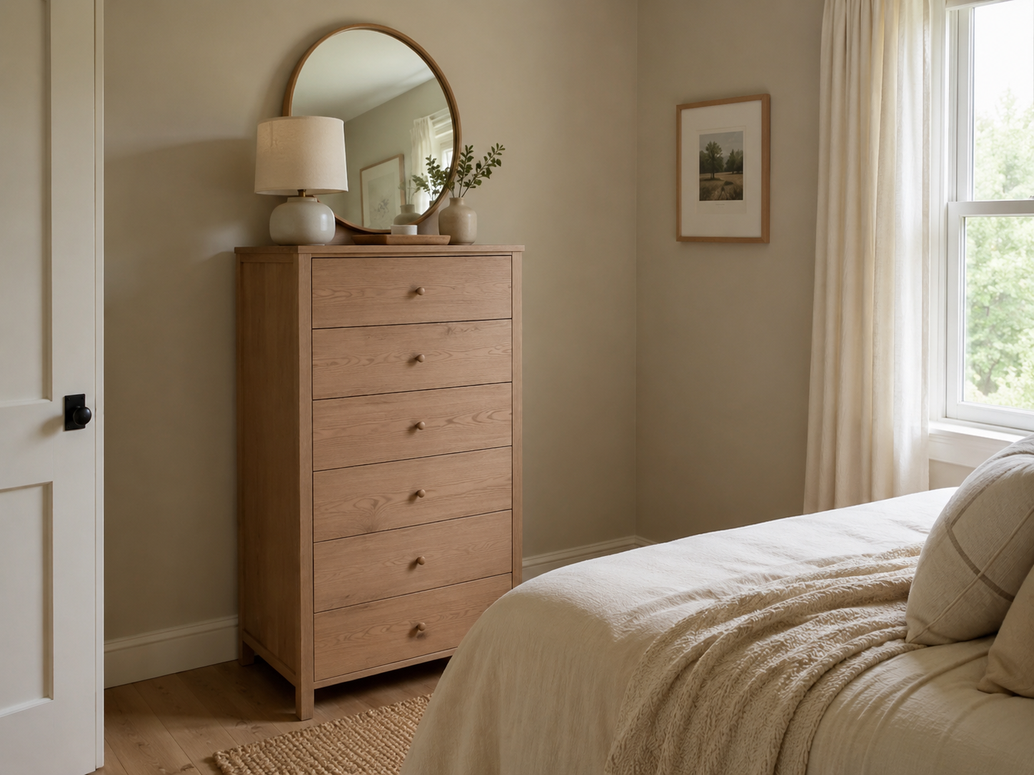 Small bedroom with a tall narrow wooden dresser, round mirror, lamp, ceramic vase, tray, and partial bed or curtain view